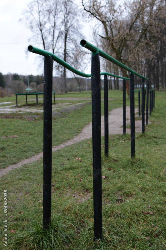 Empty old bent metal gymnastic bars on an abandoned sports field in the Park on a cloudy autumn day on green grass and bare trees background
