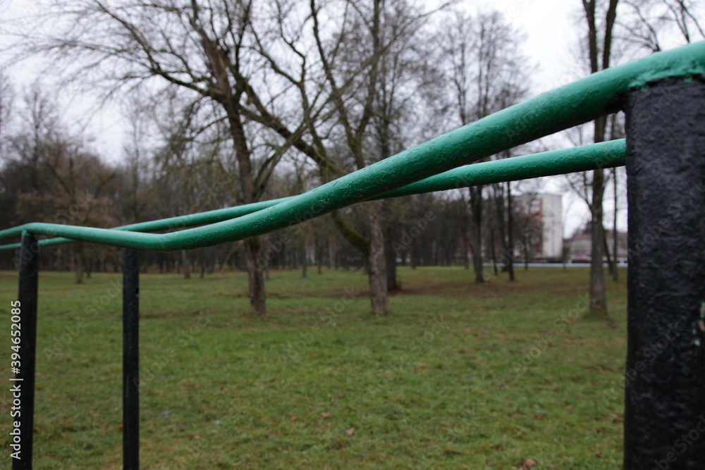 Fototapeta premium Empty old bent metal gymnastic bars close up on an abandoned sports field in the Park on a cloudy autumn day on green grass and bare trees background