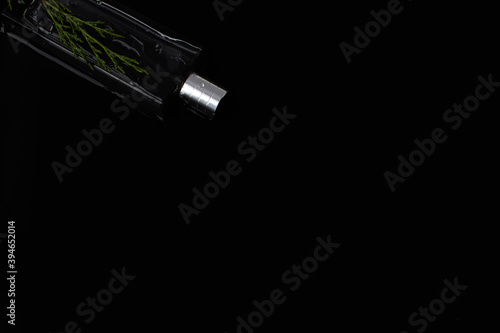 Perfume bottle on a black background with a juniper branch. The concept of freshness men's fragrance