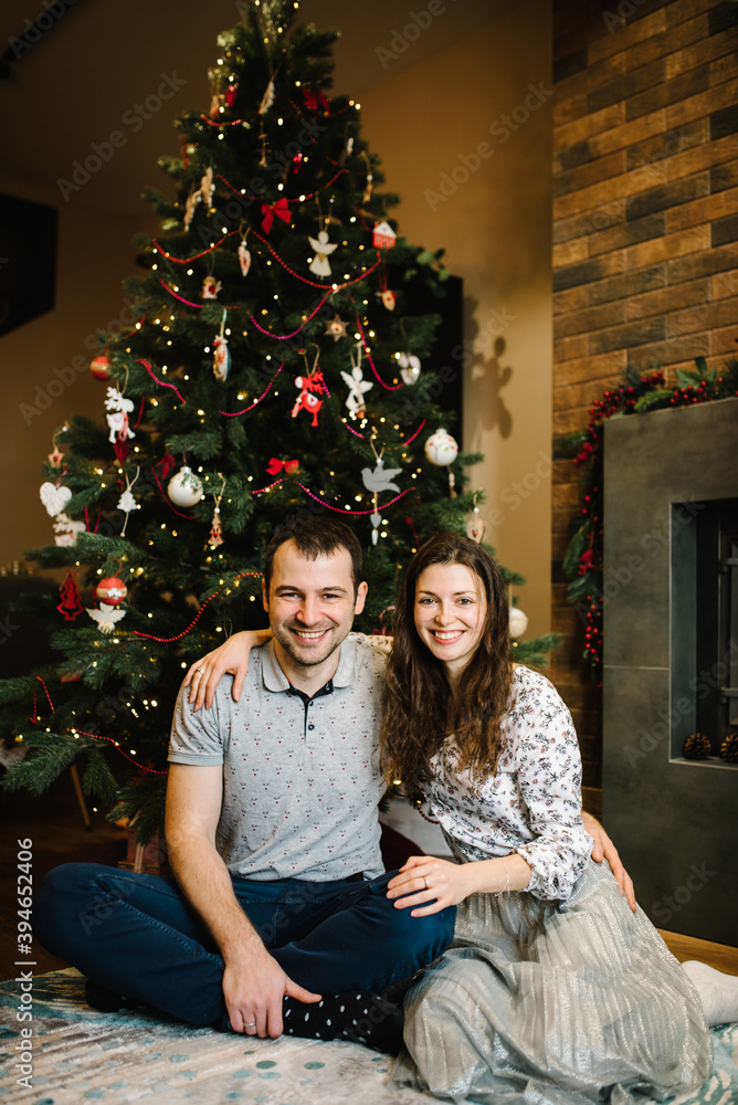 Happy couple in love sitting on the floor near the Christmas tree. Man and woman hugging. Happy winter holidays. Happy New Year and Merry Christmas.
