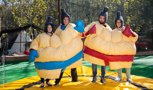 Portrait of happy adult friends having fun posing in inflatable sumo suits at outdoor amusement park
