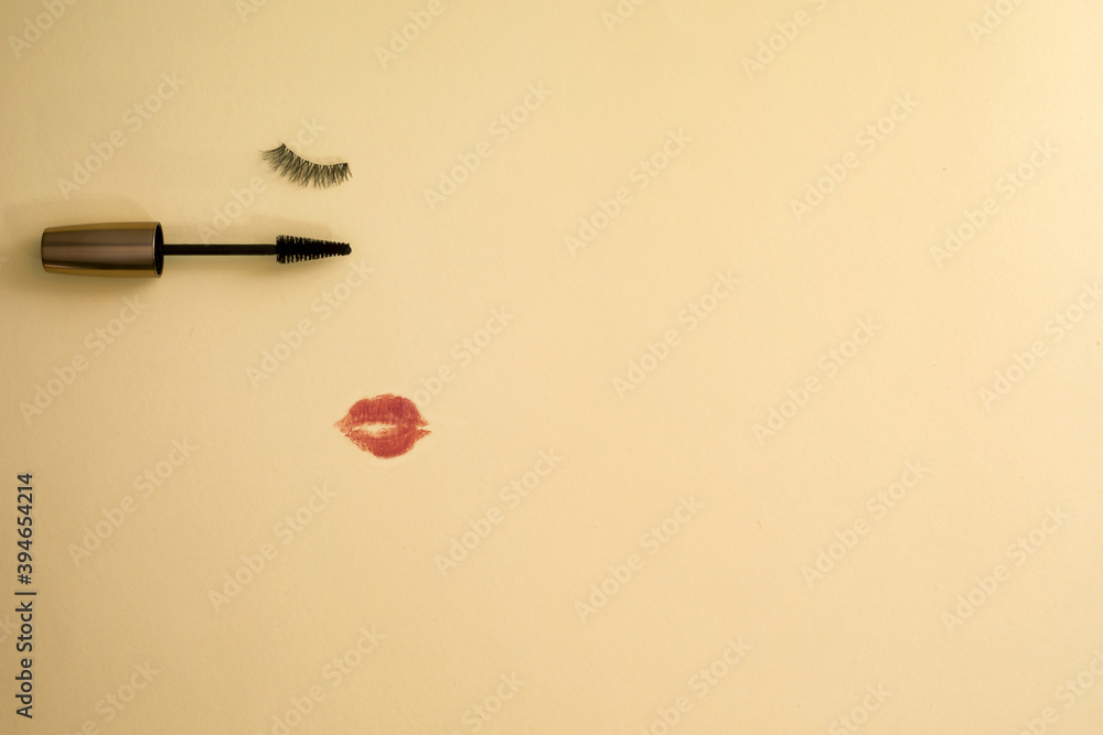 False eyelashes and a mascara wand with a red lipstick kiss mark on an orange background, with copy space. False eyelashes and a mascara wand with a red lipstick kiss mark on an orange background, with copy space.