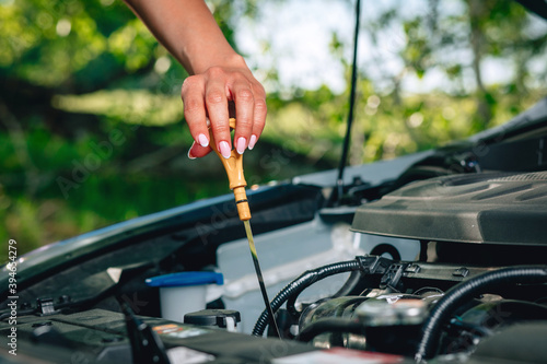 woman's hand is checking an oil in her car via an oil dipstick against the background of nature, close up
