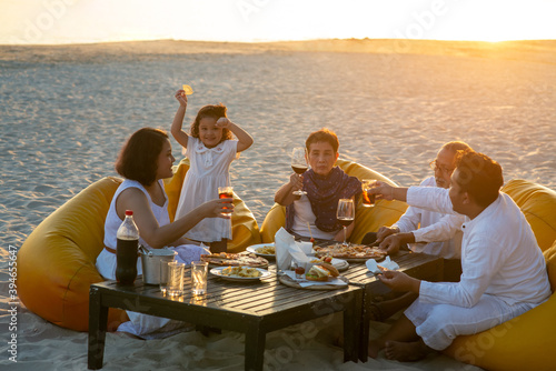 Group of multi generation Asian family enjoy dinner party together on the beach at sunset. Diverse family with child girl, adult and senior couple relax and having fun on summer holiday vacation © CandyRetriever 
