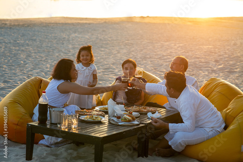Group of multi generation Asian family enjoy dinner party together on the beach at sunset. Diverse family with child girl, adult and senior couple relax and having fun on summer holiday vacation © CandyRetriever 