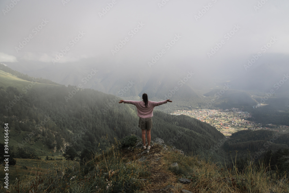 girl tourist, standing on the top of the mountain, arms are spread apart