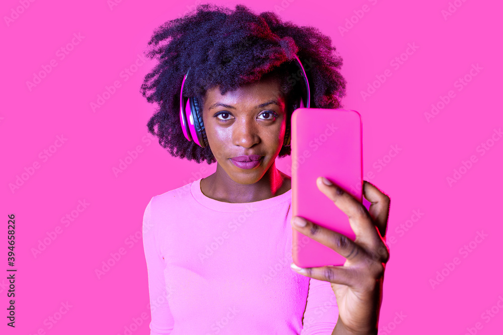 Young beautiful black woman taking selfie on pink background looking camera Young beautiful black woman taking selfie on pink background looking camera
