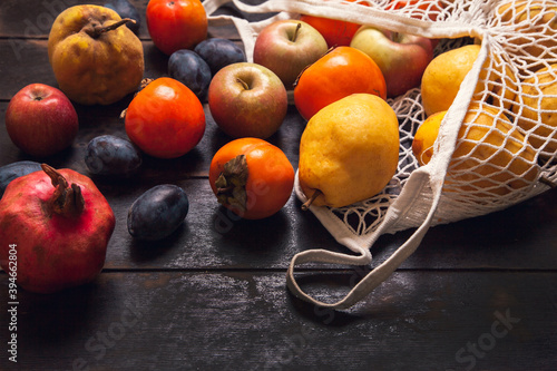 Fototapeta Naklejka Na Ścianę i Meble -  Various autumn fruits in a mesh bag on a dark wooden background