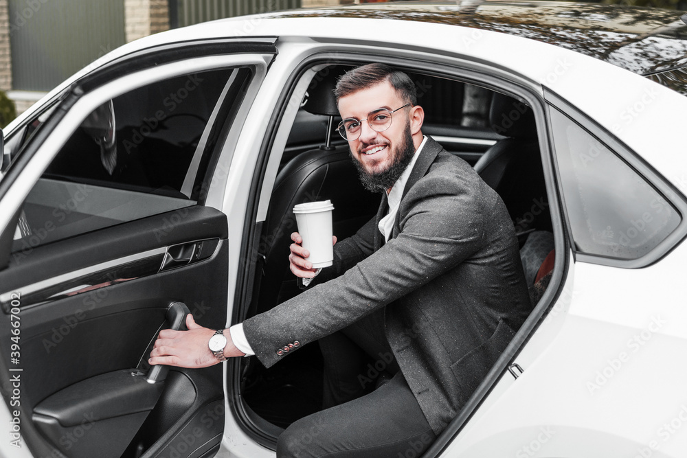 Portrait of a handsome businessman with glasses getting out of his car, smiling and looking at the camera