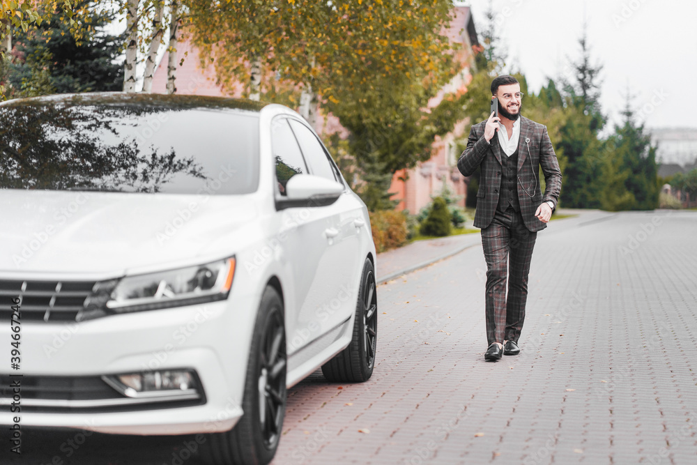 A handsome, smiling, happy, bearded man in a suit speaks on the phone going to his car A handsome, smiling, happy, bearded man in a suit speaks on the phone going to his car