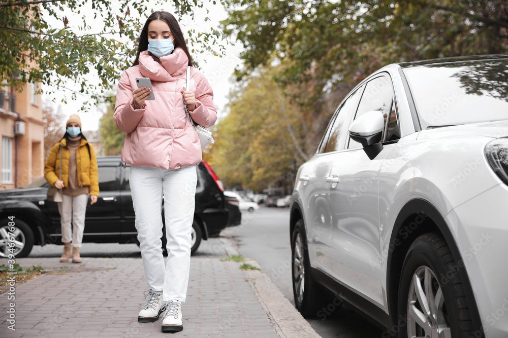 Young woman in medical face mask with smartphone walking outdoors. Personal protection during COVID-19 pandemic Young woman in medical face mask with smartphone walking outdoors. Personal protection during COVID-19 pandemic