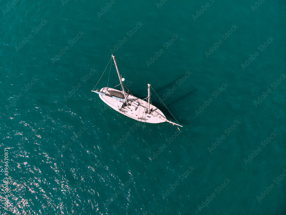 Fototapeta premium Small sail boat is sailing across the deep emerald sea. Aerial view.
