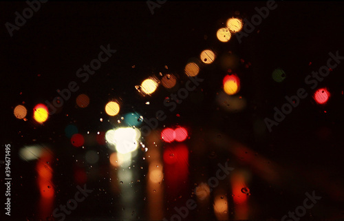 Car traffic lights bokeh through rainy window glass on black background. Defocused city night colorful round lights.