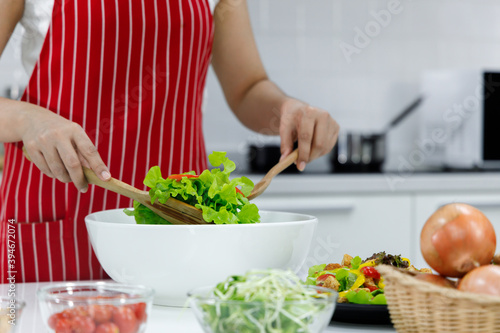 Chef mixing salad in white bowl.