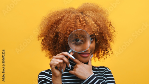 Funny young african american black woman with magnifier in hand shows eye through magnifying glass. High quality photo