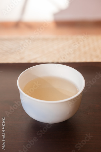 Beautiful porcelain tea cup close up shot. Hydrating pale liquor in it. Bai Hao Yin Zhen (White Hair Silver Needle) white tea from Fujian province. Vertical shot.