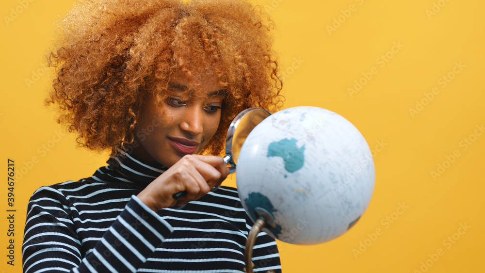Naklejka premium Young african american black woman looking at the globe through the magnifier. High quality photo