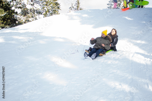 Happy young couple going down a small snowy hill on a sled