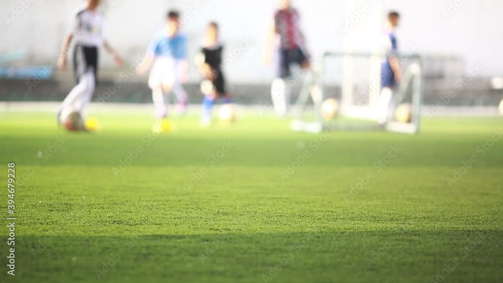 Selective focus to green artificial turf with blurry coach is coaching kid player with ball and soccer training equipment. Blurry Background football training in soccer academy. Selective focus to green artificial turf with blurry coach is coaching kid player with ball and soccer training equipment. Blurry Background football training in soccer academy.