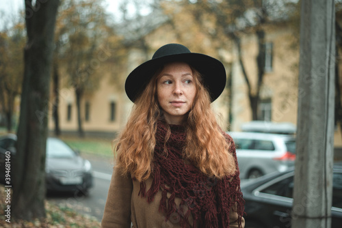 Girl with red hair in a black hat and coat in an autumn park © Hanna