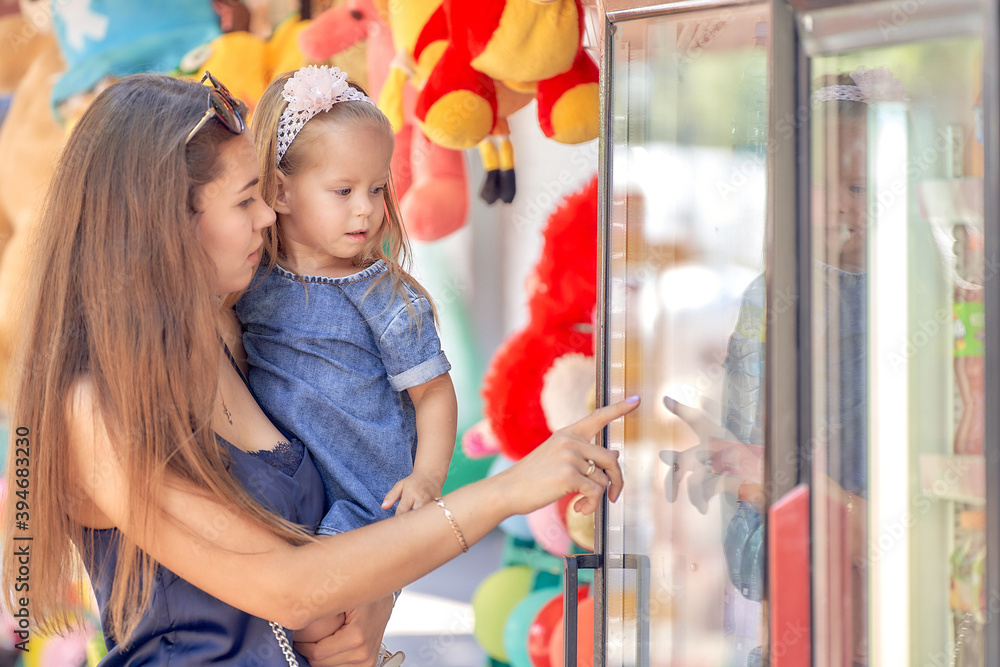 A young mother with her daughter in her arms chooses lemonade in the window of the refrigerator. Hot summer day. A young mother with her daughter in her arms chooses lemonade in the window of the refrigerator. Hot summer day.