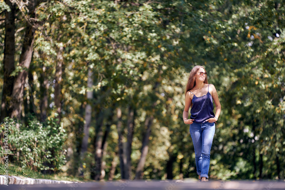 A lovely woman is walking in a park. Greenery of trees. Summer sunny day.