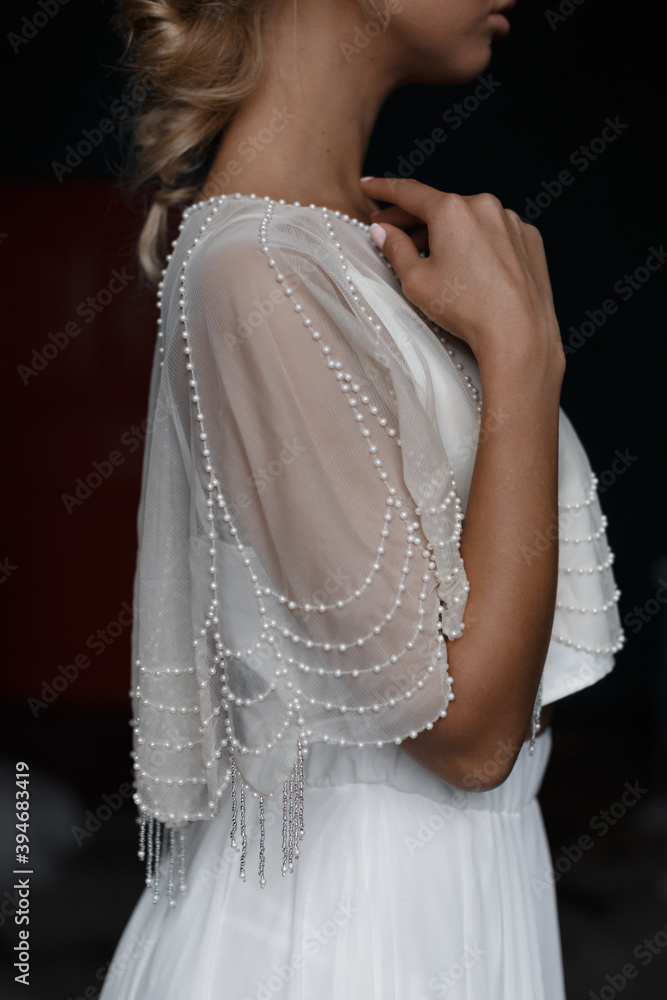 Close up photo of pretty blonde bride in white wedding dress. Beautiful marriage dress with beads. Solemn event. Waiting for the groom. Details of chic wedding dress.