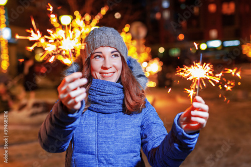 Happy woman with sparkler in winter outdoors with festive lighting, christmas evening