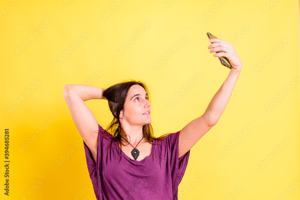 Young pretty woman takes a picture of herself with her mobile, isolated on yellow studio background. Young pretty woman takes a picture of herself with her mobile, isolated on yellow studio background.