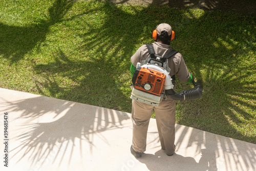 Rearview of an unknown man working in the garden with a shoulder blower machine. Mexico
