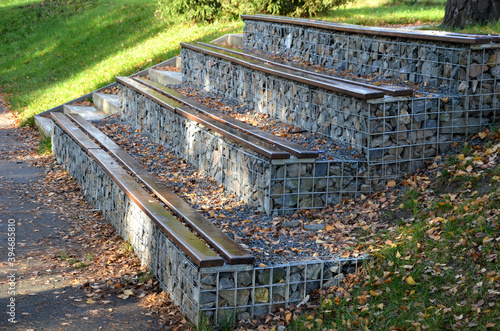 grandstand in the park by a concrete staircase made of gabion baskets with gray stones arranged inside. the seating areas of the benches are steps made of planks. photo