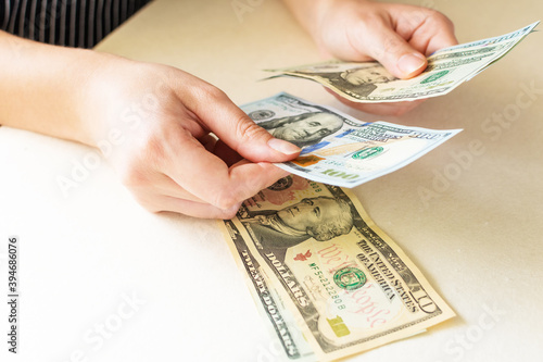 Woman's hands counting dollar bills, on white desk.