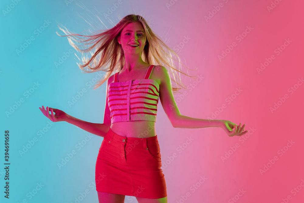 Long hair. Beautiful young girl in fashionable, romantic pink outfit on gradient pink-blue background in neon light. Half-length portrait. Copyspace for ad. Summer, fashion, beauty, emotions concept.