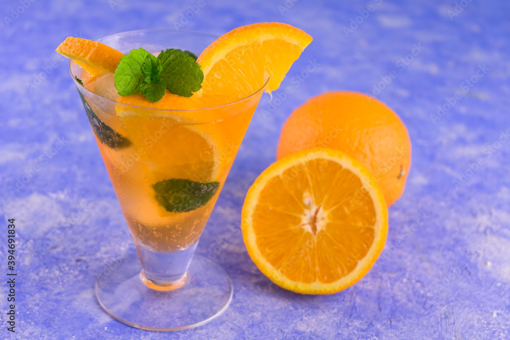 A glass of refreshing orange cocktail with mint and ice on a blue bright background. A glass of refreshing orange cocktail with mint and ice on a blue bright background.