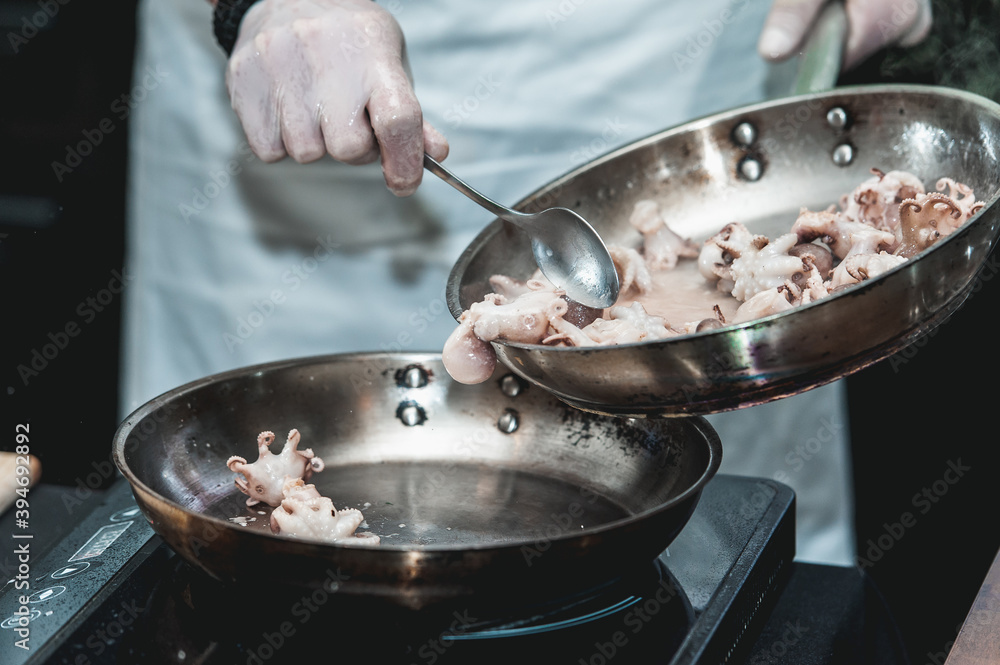 The chef cooks the small octopus on a metal frying pan