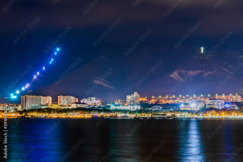 Resort city Gelendzhik with mountains and night illumination reflected in sea bay water.