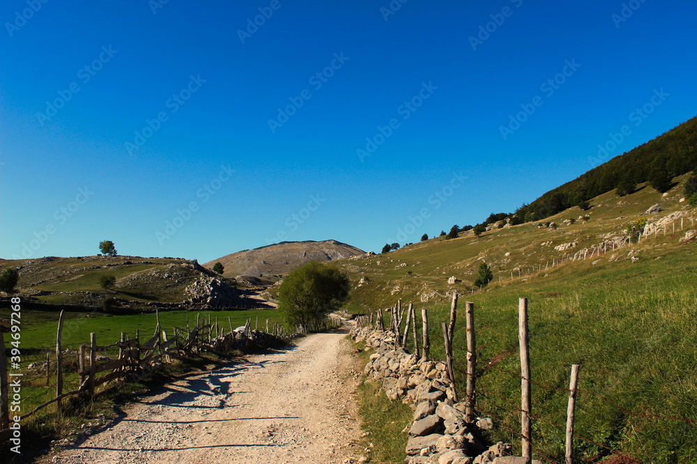 Mountain road that leads to the old Bosnian village of Lukomir. The road is surrounded by stone with wooden pillars connected by barbed wire.