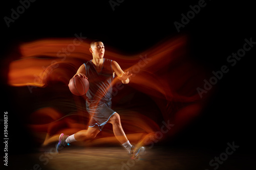 High flight. Young east asian basketball player in action and motion jumping in mixed light over dark studio background. Concept of sport, movement, energy and dynamic, healthy lifestyle.