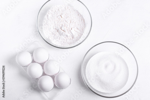 Ingredients to make sponge cake. Eggs, sugar and flour on the white table. Step by step recipe of sponge cake. Step 1. Set of white ingredients. Top view