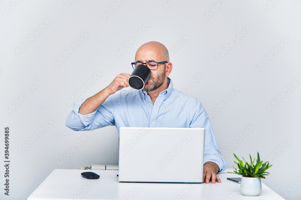 Businessman teleworking with a laptop having a coffee. Bald man with glasses Businessman teleworking with a laptop having a coffee. Bald man with glasses
