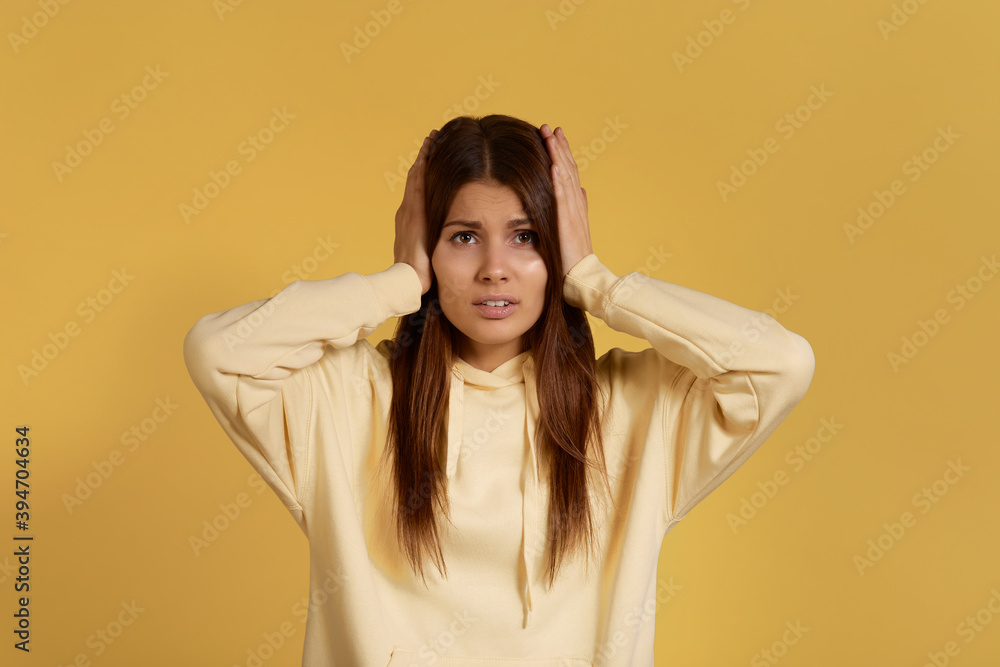 Want silence and calm atmosphere. Tired beautiful caucasian woman in yellow hoodie plugging her ears with palms, being annoyed with noise and colleagues conversations. Isolated on a yellow background. Want silence and calm atmosphere. Tired beautiful caucasian woman in yellow hoodie plugging her ears with palms, being annoyed with noise and colleagues conversations. Isolated on a yellow background.