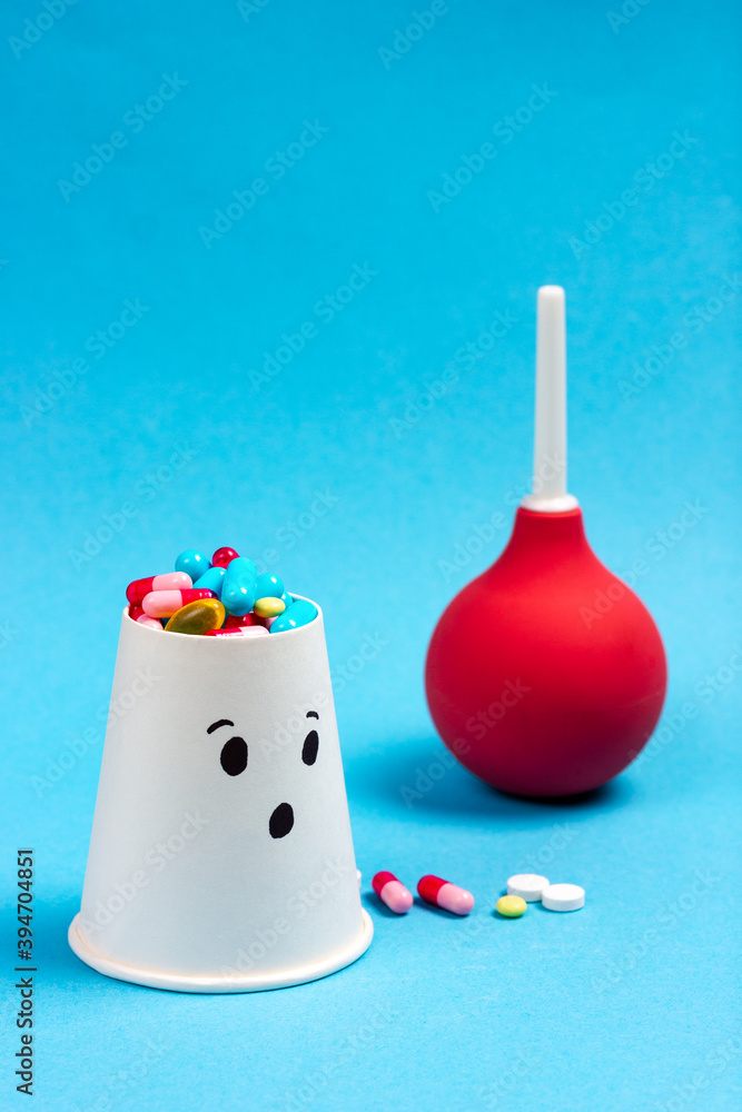 Patient with pills - colored medical pills on a blue background. In the background is a medical enema. The theme of the treatment of food poisoning, flu.