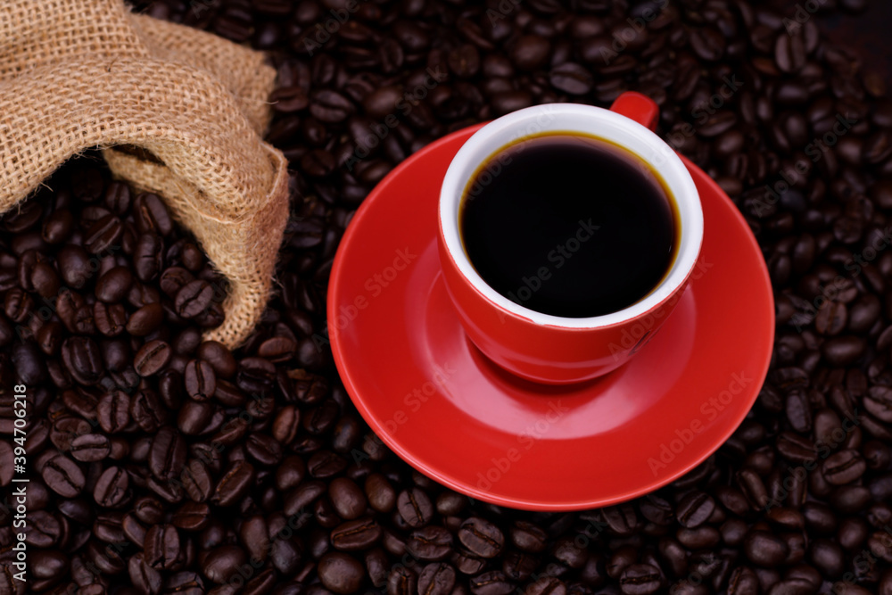Fototapeta premium Fresh black coffee, a needle in a red coffee cup and fragrant roasted coffee beans, placed on a dark table Espresso coffee - Top view with copy space