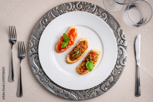 Crostini with meat sauce, tomatoes, basil and peppers on a white plate