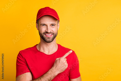 Photo of cheerful bearded guy direct finger empty space wear red t-shirt headwear isolated yellow color background