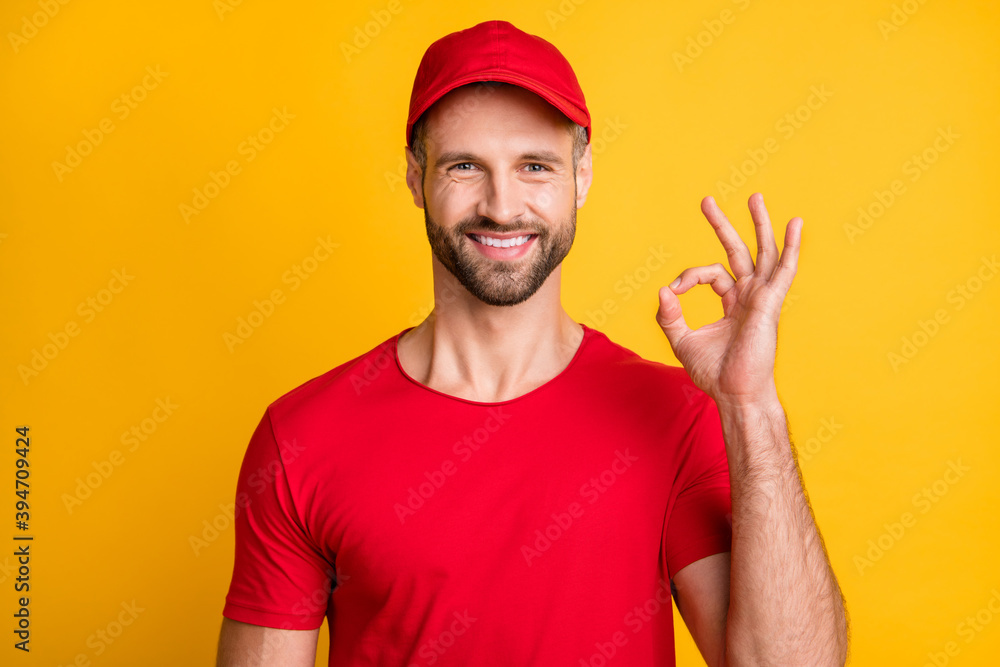 Photo of funny bristled guy showing fingers okey beaming white smile wear red t-shirt cap isolated yellow color background
