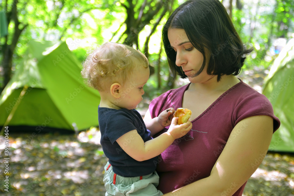 Travel with small children. Young woman with baby in front of the tent in the wood. Travel with small children. Young woman with baby in front of the tent in the wood.
