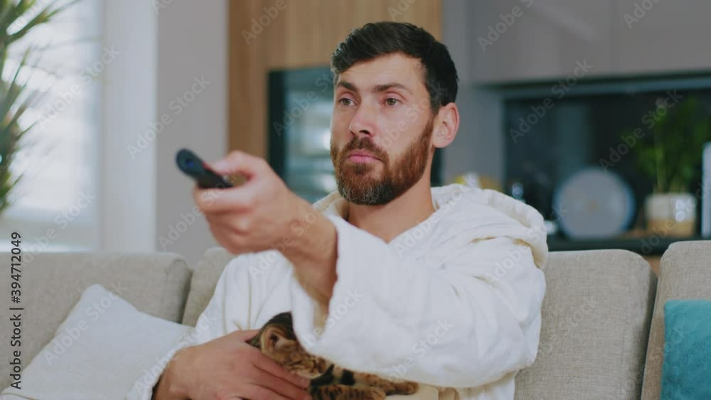 Wonder young man with cat watching TV. Sitting on sofa smiling at home. Relaxation cinema channels resting. Portrait. Close up. Slow motion. Wonder young man with cat watching TV. Sitting on sofa smiling at home. Relaxation cinema channels resting. Portrait. Close up. Slow motion.