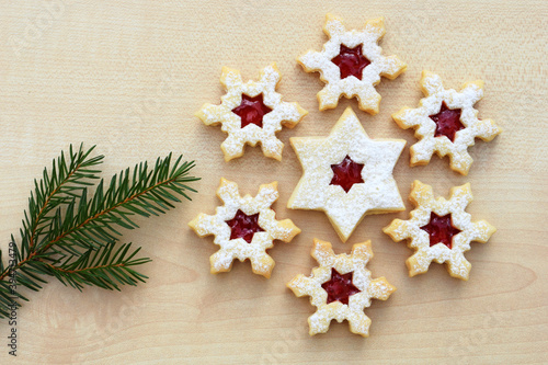Homemade linzer cookies in a shape of snowflakes and star filled with strawberry jam, spruce twig, top view