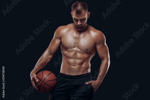 Portrait of a very muscular naked man playing basketball isolated on black background